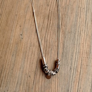 May include: A silver chain necklace with a silver pendant and multiple silver rings attached to the chain.