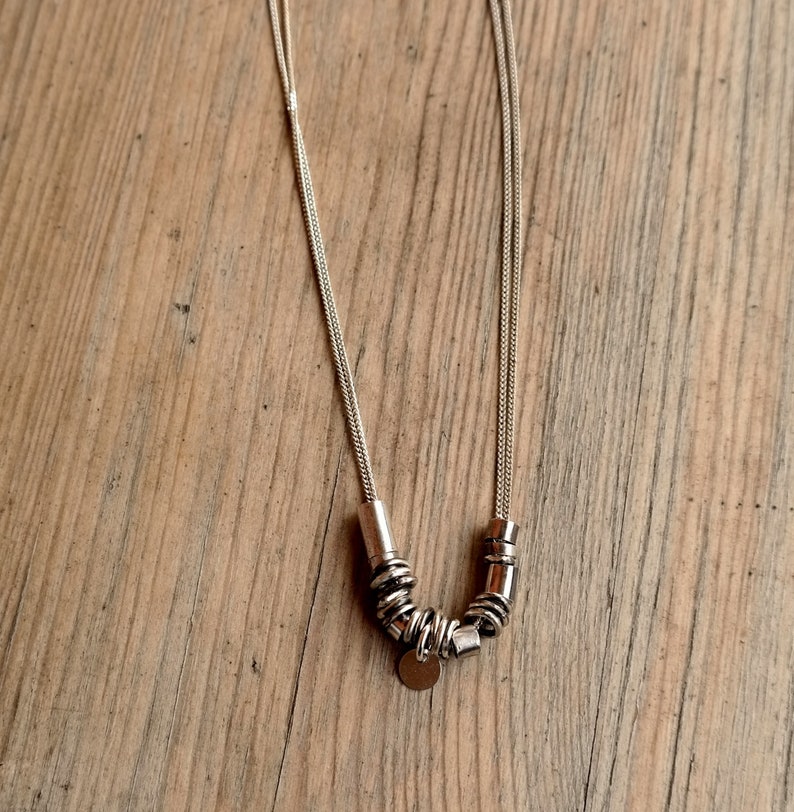 May include: A silver chain necklace with a silver pendant and multiple silver rings attached to the chain.