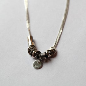 May include: A silver necklace with a chain and a pendant made of multiple silver rings. The pendant has a small tag with the number "925" on it.
