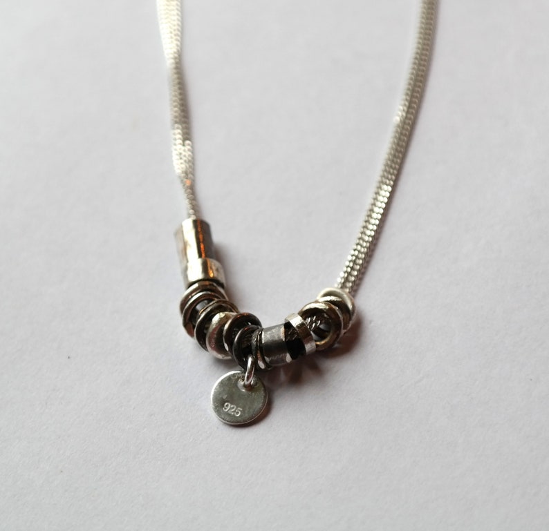 May include: A silver necklace with a chain and a pendant made of multiple silver rings. The pendant has a small tag with the number "925" on it.