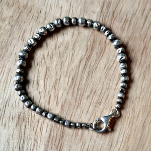 May include: A silver bracelet with a clasp closure. The bracelet is made of small, round beads.