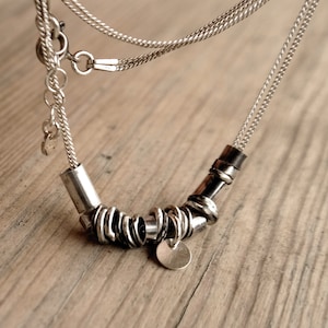 May include: A silver necklace with a chain and a pendant made of multiple silver rings. The pendant has a circular charm.