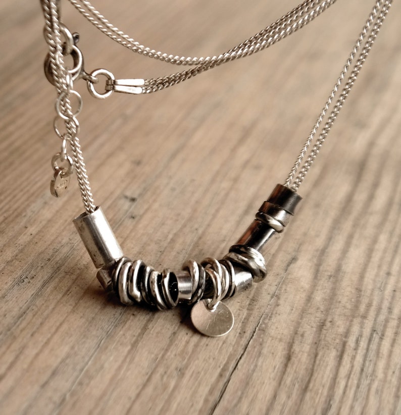 May include: A silver necklace with a chain and a pendant made of multiple silver rings. The pendant has a circular charm.
