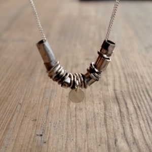 May include: A silver necklace with a unique design featuring multiple interconnected rings and a small circular pendant.
