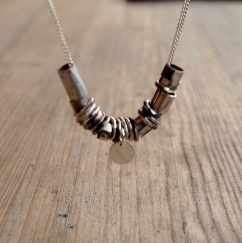 May include: A silver necklace with a unique design featuring multiple interconnected rings and a small circular pendant.