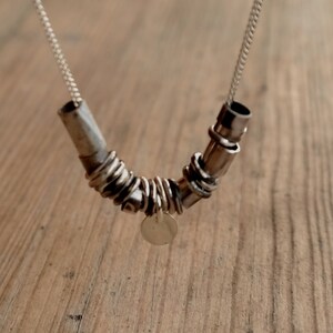 May include: A silver necklace with a unique design featuring multiple interconnected rings and a small circular pendant.
