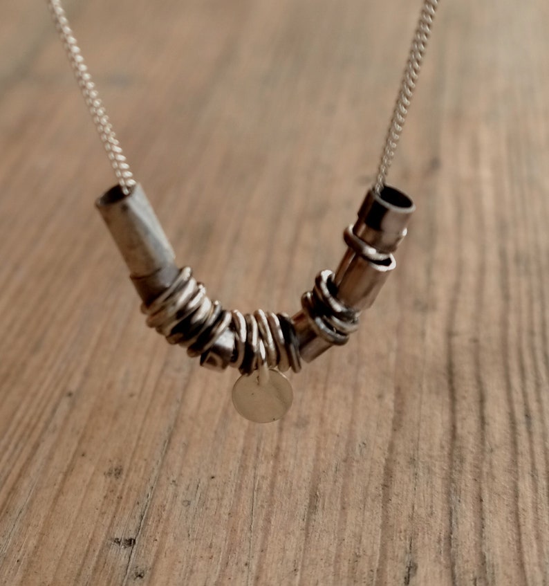 May include: A silver necklace with a unique design featuring multiple interconnected rings and a small circular pendant.