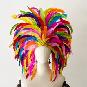 May include: A vibrant, multi-colored feather headdress featuring a dense arrangement of long, upright feathers in shades of red, orange, yellow, green, blue, and purple. A central gold-toned, star-shaped embellishment sits at the front base.