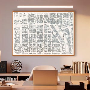 May include: A modern home office with a large wooden desk, a laptop, and a framed map on the wall. The room features a neutral color palette, a desk lamp, and a bookshelf. Overhead, there are linear pendant lights.