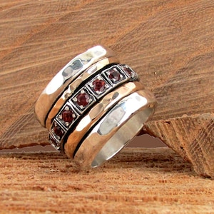 May include: A silver and gold ring with a band of red gemstones. The ring is made of multiple bands that spin around each other.