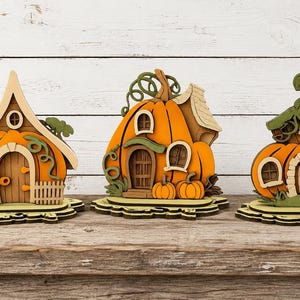 May include: Three decorative wooden pumpkin-shaped houses featuring layered designs in shades of orange, brown, and green. Each structure includes detailed cutouts of doors, windows, and vines, all mounted on individual scalloped wooden bases.