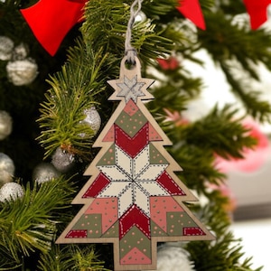 May include: Wooden Christmas tree ornament with a patchwork design. The ornament features a star at the top and is decorated with red, white, pink, and green geometric shapes. It hangs from a natural twine string.