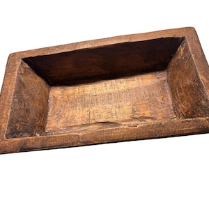 May include: A rectangular, rustic wooden bowl with a dark brown finish. The bowl has a shallow, open interior and is made from a single piece of wood. The edges are slightly rough, giving it a handcrafted appearance. This decorative bowl is ideal for home decor.