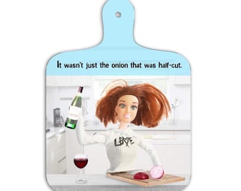 May include: A light blue, wooden cutting board with a handle, featuring a doll holding a wine bottle and a glass of red wine. The text on the board reads, "It wasn't just the onion that was half-cut."