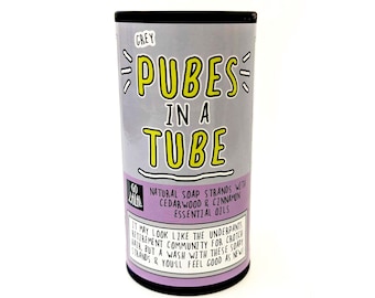 May include: A cylindrical container with the text "PUBES IN A TUBE" in yellow letters on a grey background. The container also has text that reads "NATURAL SOAP STRANDS WITH CEDARWOOD & CINNAMON ESSENTIAL OILS". The container is black on the top and bottom.