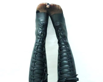 May include: Black knee-high boots with laces and a black bow at the top. The boots are worn with black polka dot tights.