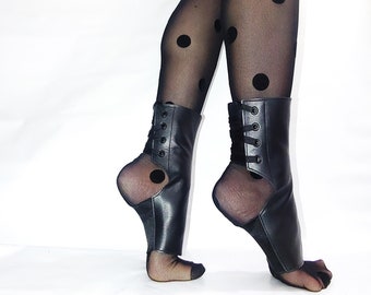 May include: Black leather ankle boots with laces up the back. The boots are worn over sheer black tights with black polka dots.