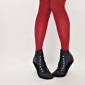 May include: A pair of black ankle boots with white laces and red tights. The boots have a unique design with a curved sole and are made of a soft, textured material. The tights are a solid, vibrant red color.