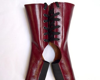 May include: A pair of burgundy leather boots with black laces and a cut-out design on the back. The boots have a black elastic band at the top of the shaft.