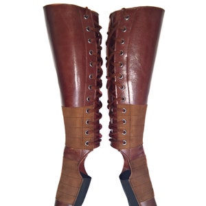 May include: A pair of brown leather boots with laces up the back. The boots have a brown suede panel and a black sole.