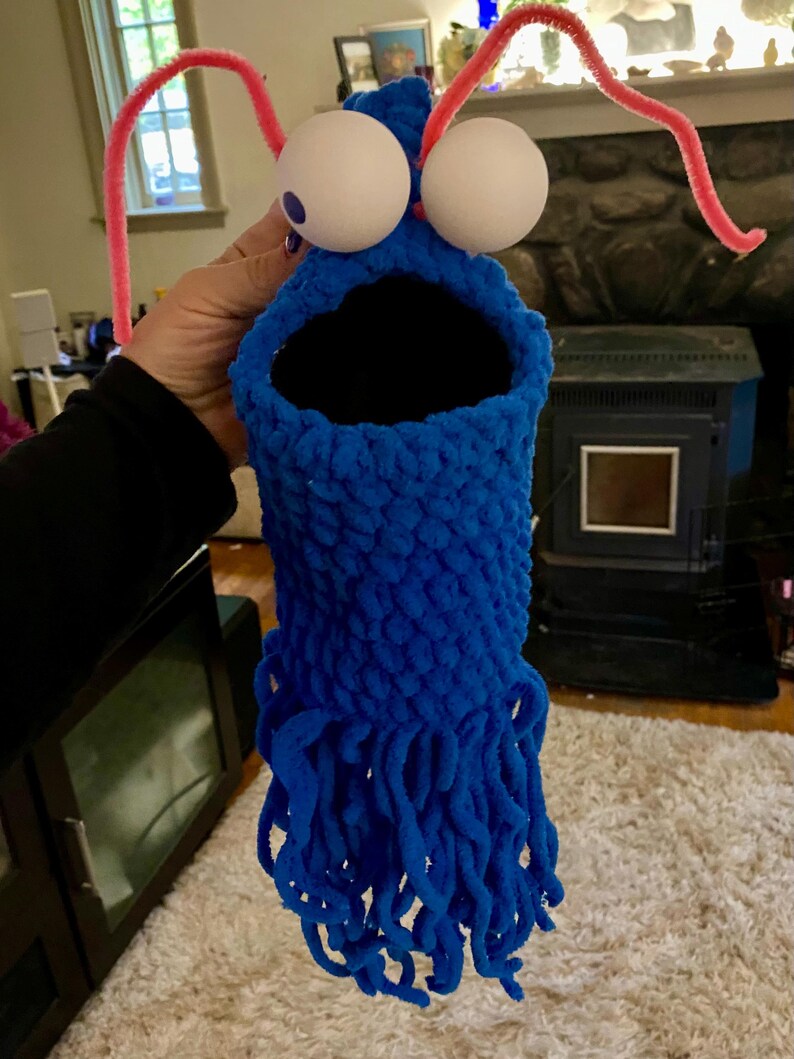 May include: A blue crocheted puppet with large white googly eyes and pink pipe cleaner antennae. The puppet has a large open mouth and a long, shaggy blue beard.