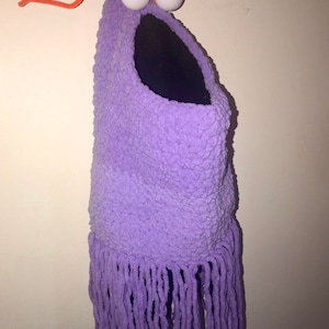 May include: A purple crocheted monster with a large mouth and googly eyes. The monster has long purple fringe hanging from the bottom.