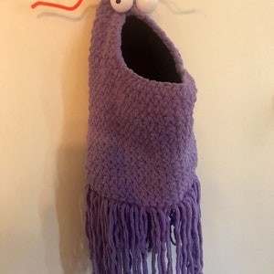 May include: Purple crocheted hanging toy with a large mouth and googly eyes. The toy has a fringe at the bottom and red pipe cleaner antennae.