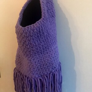 May include: Purple crocheted monster toy with googly eyes and orange pipe cleaner antennae. The monster has a large open mouth and a fringe of yarn around the bottom.