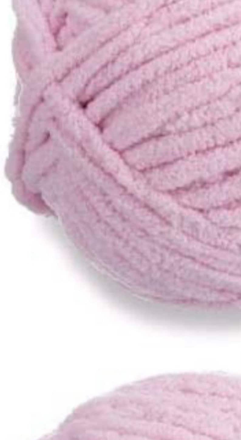 May include: A close-up of a ball of soft, light pink yarn. The yarn is made of a fuzzy, chenille-like material.