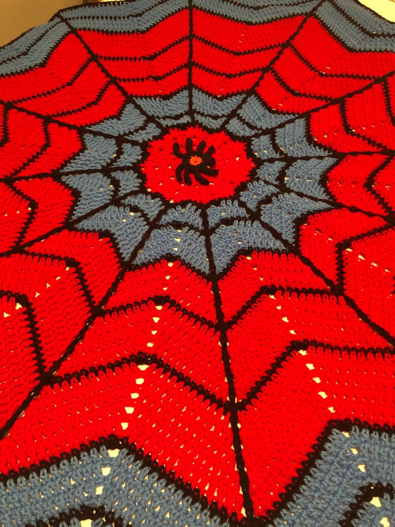 May include: A red and blue crocheted blanket with a black spider web design. The center of the web features a black spider with a red body.