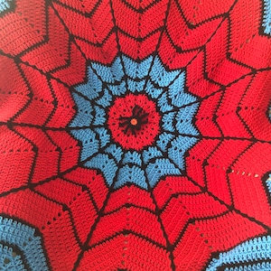 May include: A crocheted blanket with a red, blue, and black spiderweb design.