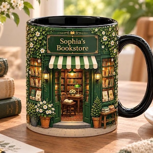 Puede incluir: Una taza de cerámica negra con una ilustración detallada de una fachada verde con el texto Sophia's Bookstore. El diseño incluye un toldo a rayas, faroles brillantes, estanterías llenas de libros, una silla de madera y flores blancas.