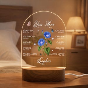 May include: An arched clear acrylic plaque with a wooden base featuring blue morning glory flowers, butterflies, and the text "You Are" followed by inspirational words and Bible verses, with the name "Sophia" printed at the bottom in white.