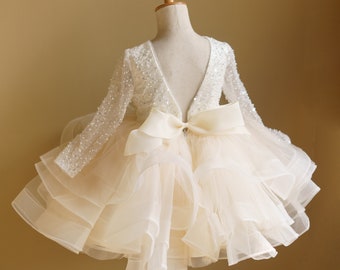 May include: A white tulle dress with a sequined bodice and a large bow in the back. The dress is on a mannequin.