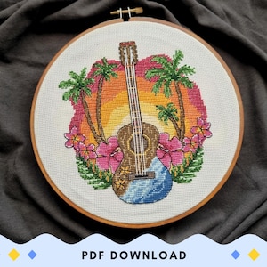 Könnte beinhalten: Ein Kreuzstich-Stickrahmen mit einer Gitarre, Palmen und tropischen Blumen vor einem Sonnenuntergang. Die Gitarre ist braun mit blauen Akzenten, und die Blumen sind rosa. Die Stickerei befindet sich in einem Holzrahmen.