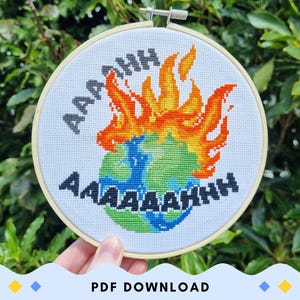 May include: A white embroidery hoop with a cross-stitch design of a burning Earth with the text "AAAAAHHH" around it.