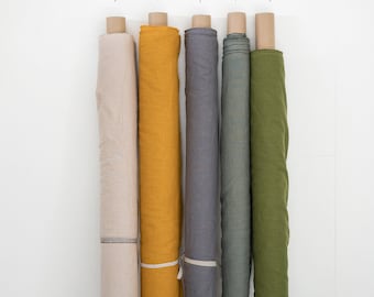 May include: Six rolls of fabric in different colors, including beige, saffron, dark grey, light moss green, and deep moss green. The fabric rolls are arranged vertically and are tied with white string.