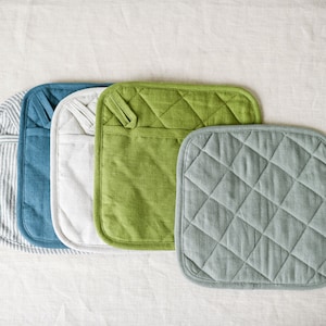 Può includere: Cinque presine imbottite in diversi colori: grigio, blu, bianco, verde e grigio chiaro. Le presine sono allineate in fila.