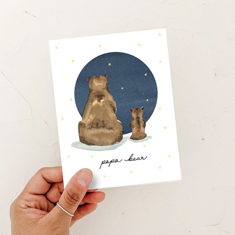 May include: A white card with a blue circle and two brown bears looking up at the stars. The text "papa bear" is written in black cursive at the bottom of the card.