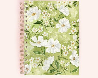 May include: A spiral-bound notebook featuring a floral design. The cover showcases a watercolor pattern of white flowers and green leaves against a light green background. The spiral binding is gold-colored.