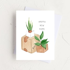 Peut inclure: Une carte de v&oelig;ux avec une illustration aquarelle de deux plantes en pot dans des bo&icirc;tes en carton. Le texte sur la carte est "Happy New Home".