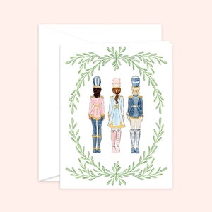 May include: Three female figures dressed as toy soldiers, standing in a row, facing away from the viewer. They are wearing blue and pink uniforms with gold accents and white hats. The figures are surrounded by a green wreath.