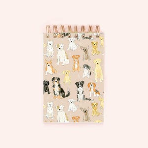 May include: Spiral-bound notepad featuring a beige background with watercolor illustrations of various dog breeds. The dogs are in different poses and colors, including white, brown, black, and yellow. The spiral binding is gold-colored.