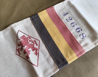 May include: A white canvas fabric strip featuring a red embroidered lion inside a diamond shape, a vertical tricolor band in dark gray, yellow, and pink, and the blue embroidered number 42668 stitched onto the right side of the textile.