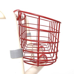 May include: Red metal bicycle basket with a curved shape and a wire mesh design. The basket is attached to a white bicycle frame.