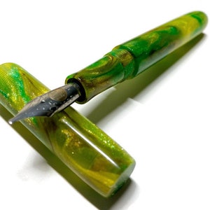 Puede incluir: Una pluma estilogr&aacute;fica verde y dorada con una plumilla de metal. La pluma est&aacute; hecha de resina marmoleada con un acabado brillante.