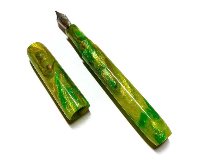 Puede incluir: Una pluma estilogr&aacute;fica verde y dorada con un dise&ntilde;o de m&aacute;rmol. La pluma est&aacute; tapada y la tapa est&aacute; a un lado.