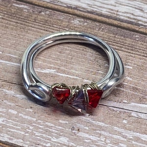 May include: A silver ring with red and purple crystals wrapped in wire.