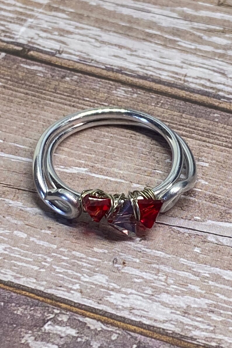 May include: A silver ring with red and purple crystals wrapped in wire.