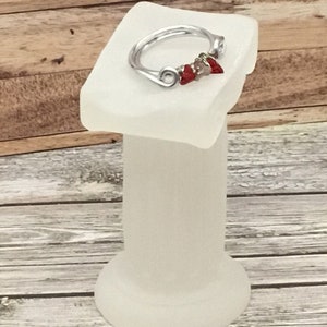 May include: A silver wire ring with three red and silver beads. The ring is displayed on a white pedestal.